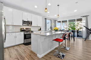 Kitchen featuring appliances with stainless steel finishes, a breakfast bar area, light stone counters, white cabinetry, and a center island with sink