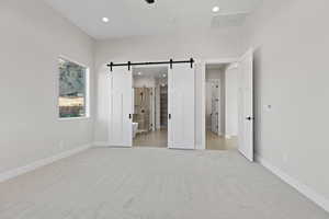 Unfurnished bedroom with light colored carpet, a barn door, recessed lighting, a ceiling fan, and ensuite bath