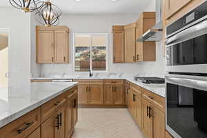 Kitchen featuring stainless steel appliances, hanging light fixtures, light stone countertops, and a chandelier