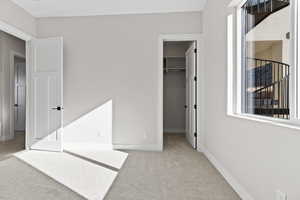 Unfurnished bedroom featuring a walk in closet, light colored carpet, and multiple windows