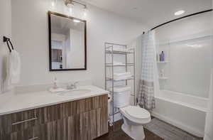 Bathroom with dark wood-type flooring, shower / bath combination with curtain, and vanity