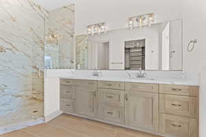 Full bath with a marble finish shower, double vanity, and a walk in closet