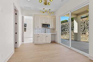 Kitchen with decorative backsplash, light brown cabinets, a chandelier, stainless steel microwave, and light wood-style floors