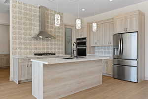 Kitchen featuring light brown cabinets, stainless steel appliances, wall chimney range hood, backsplash, and pendant lighting