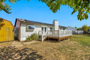 Back of property featuring roof mounted solar panels, a chimney, brick siding, a fenced backyard, and a wooden deck