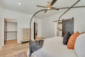 Bedroom with a barn door, recessed lighting, light wood-type flooring, wood walls, and a spacious closet