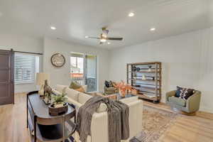 Living room featuring light wood-type flooring, recessed lighting, a barn door, and a ceiling fan