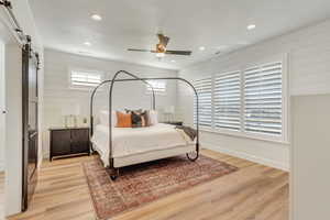 Bedroom featuring a barn door, light wood-style floors, ceiling fan, recessed lighting, and a textured ceiling