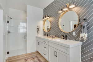 Bathroom with a shower stall, double vanity, and light wood-style flooring