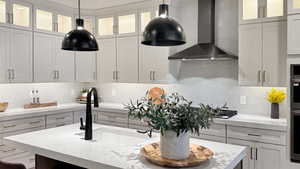 Kitchen with wall chimney range hood, backsplash, glass insert cabinets, and light stone counters