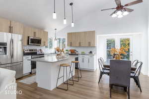 Kitchen with high vaulted ceiling, stainless steel appliances, decorative backsplash, hanging light fixtures, and light brown cabinets