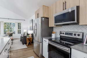 Kitchen featuring stainless steel appliances, lofted ceiling, open floor plan, tasteful backsplash, and light brown cabinetry