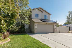 Traditional-style home with a gate, solar panels, driveway, an attached garage, and a shingled roof