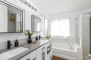Bathroom featuring double vanity, a shower stall, a bath, and dark wood-style flooring