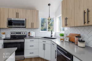 Kitchen with stainless steel appliances, light stone countertops, pendant lighting, backsplash, and light wood finished floors