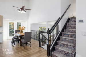 Dining space featuring a towering ceiling, light wood finished floors, plenty of natural light, a ceiling fan, and stairs