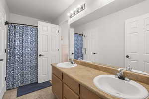 Full bath with double vanity, light tile patterned flooring, and a shower with shower curtain