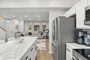 Kitchen with white cabinets, light wood-style floors, open floor plan, light stone countertops, and recessed lighting