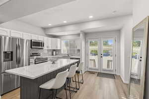 Kitchen with stainless steel appliances, white cabinetry, light wood-type flooring, a kitchen breakfast bar, and decorative backsplash