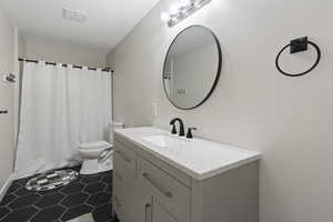 Bathroom featuring vanity, dark tile patterned flooring, shower / bath combo, and a textured wall