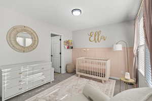 Bedroom with carpet floors, a crib, a wainscoted wall, and a decorative wall