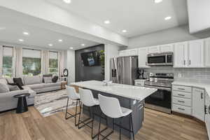 Kitchen featuring appliances with stainless steel finishes, white cabinetry, a kitchen breakfast bar, recessed lighting, and light stone countertops