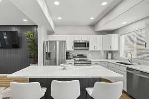 Kitchen with light stone countertops, appliances with stainless steel finishes, white cabinets, a center island, and recessed lighting
