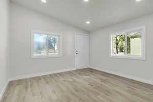 Spare room featuring recessed lighting, healthy amount of natural light, vaulted ceiling, and light wood-style floors