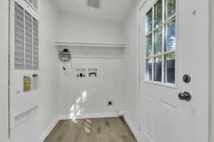 Washroom with a heating unit, light wood-style flooring, hookup for a washing machine, and hookup for an electric dryer