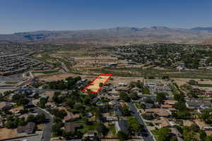 Aerial view of property and surrounding area with nearby suburban area, property parcel outlined, and a mountain backdrop