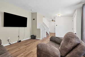 Living room with wood finished floors, stairway, a ceiling fan, and a textured ceiling