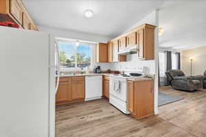 Kitchen with white appliances, light wood finished floors, under cabinet range hood, open floor plan, and light countertops