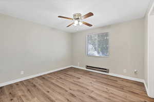 Spare room with baseboard heating, light wood-style floors, and ceiling fan