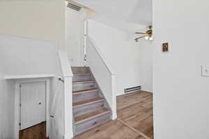 Stairs featuring wood finished floors, a baseboard radiator, and a ceiling fan