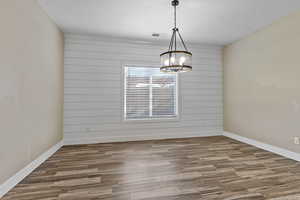 Spare room with wooden walls, wood finished floors, a chandelier, and an accent wall