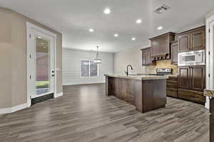 Kitchen featuring a textured ceiling, an island with sink, decorative light fixtures, recessed lighting, and dark wood-type flooring
