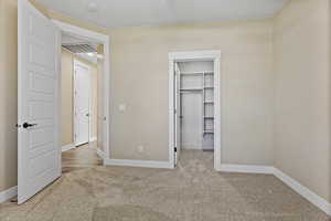 Unfurnished bedroom featuring light carpet and a walk in closet
