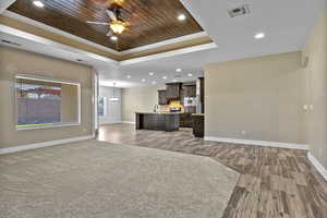 Living area featuring a tray ceiling, wooden ceiling, recessed lighting, ceiling fan, and crown molding
