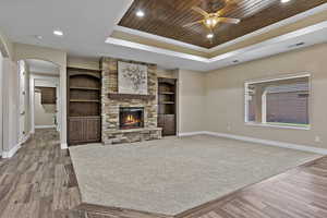 Unfurnished living room featuring wood ceiling, a tray ceiling, light wood finished floors, recessed lighting, and arched walkways
