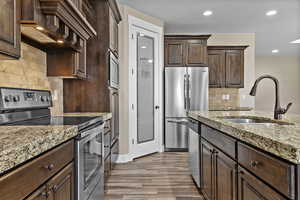 Kitchen featuring dark brown cabinets, stainless steel appliances, backsplash, premium range hood, and recessed lighting