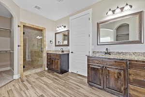 Full bathroom featuring a stall shower, two vanities, a walk in closet, and light wood-style flooring