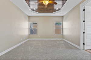 Unfurnished room featuring a tray ceiling, light carpet, wood ceiling, a ceiling fan, and crown molding