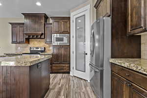 Kitchen featuring tasteful backsplash, dark brown cabinetry, appliances with stainless steel finishes, light wood-style flooring, and a textured ceiling