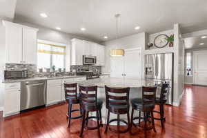 Kitchen featuring appliances with stainless steel finishes, white cabinetry, a kitchen island, light stone countertops, and dark wood-style floors