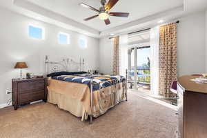 Carpeted bedroom with a tray ceiling, access to outside, and a ceiling fan