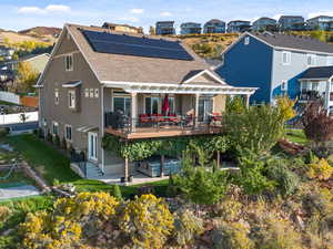 Rear view of house featuring a wooden deck, a patio area, a residential view, roof with shingles, and solar panels