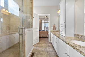 Ensuite bathroom featuring double vanity, a stall shower, a ceiling fan, and light tile patterned flooring