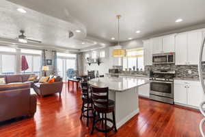 Kitchen featuring stainless steel appliances, hanging light fixtures, a kitchen island, white cabinetry, and backsplash