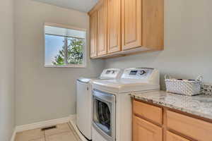 Laundry area featuring washer and clothes dryer, light tile patterned floors, and cabinet space