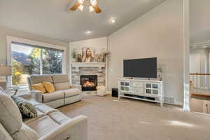 Carpeted living room featuring vaulted ceiling, a ceiling fan, a stone fireplace, and recessed lighting